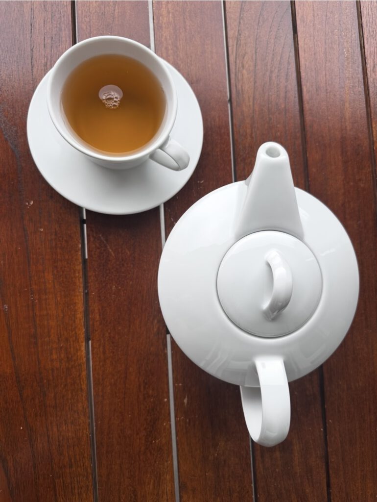 Tasse Jasmintee und weiße Teekanne auf einem Holztisch im Tessin